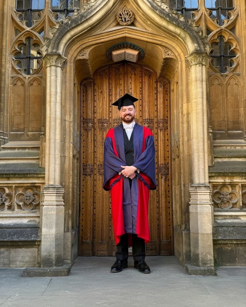 Dr Peter McCann Strain in cap and ceremonial robes framed by the gothic stone arch of the Bodleian Library doorway